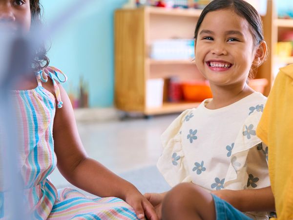 Children sitting together, one smiling brightly in a colorful classroom.