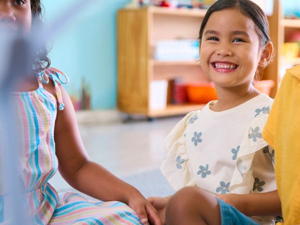 Children sitting together, one smiling brightly in a colorful classroom.