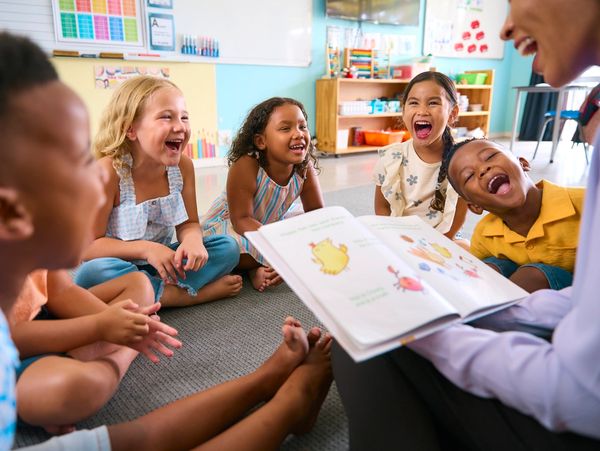 Image of children laughing as teacher reads them a book