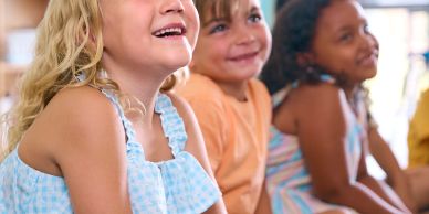 Three children smiling and sitting close together in a bright indoor setting.