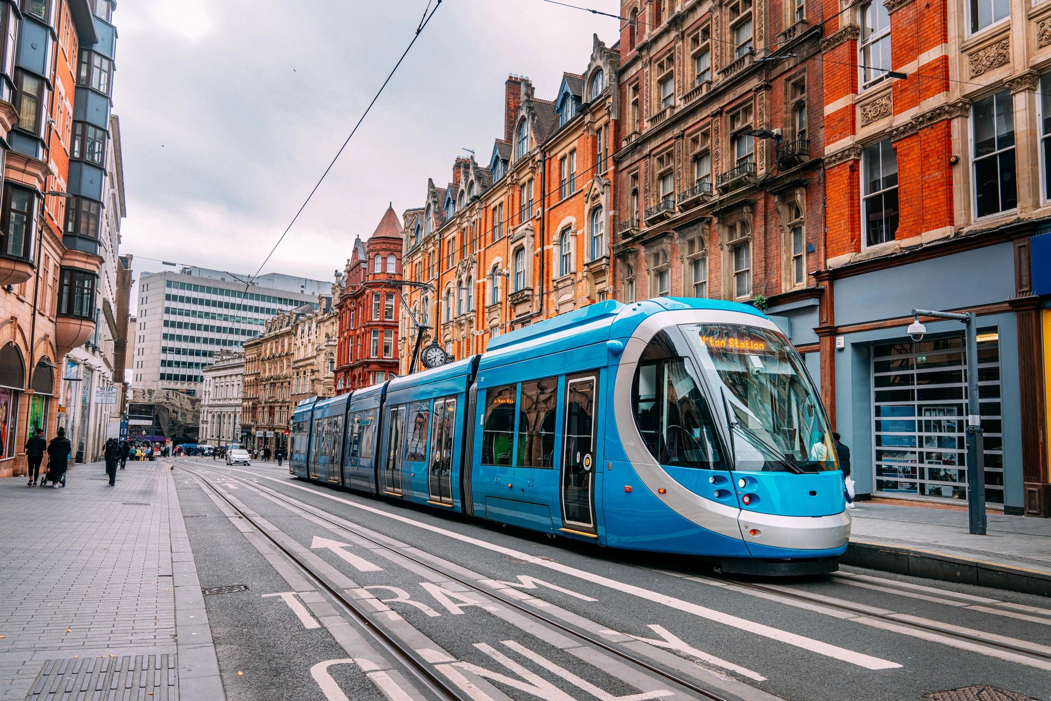 Modern blue tram traveling through a historic city street with red brick buildings.