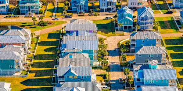 Aerial view of a coastal neighborhood with blue and gray houses under bright sunlight.
