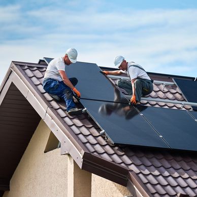 Two workers installing solar panels on a roof.