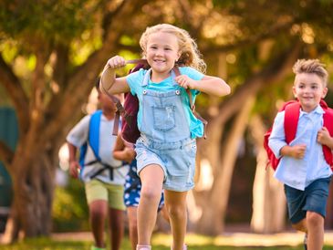 Happy children with backpacks running outdoors on a sunny day.