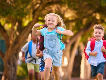 Happy children with backpacks running outdoors on a sunny day.