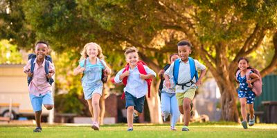 Group of happy children running outdoors with backpacks on a sunny day.