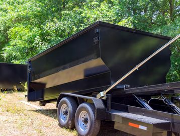 Black dump trailer parked outdoors on a sunny day.