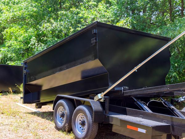 Black dump trailer in a wooded area.