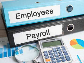 two binders stacked on top each other one labled employees, one payroll. with a calculator. 