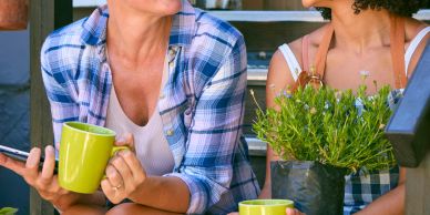 Two people chatting with green mugs and a potted plant.