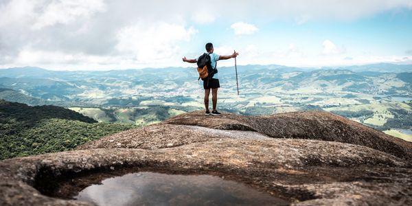 Man standing on a mountain peak overlooking the valley with arms outstretched.