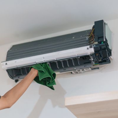 Person cleaning an open air conditioner with a green cloth.