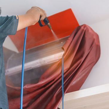 A person cleaning an air conditioning unit with a spray tool.