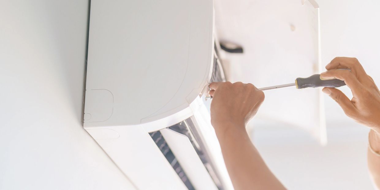 Technician repairing a wall-mounted air conditioner with a screwdriver.