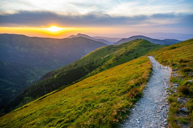 Sunset over a mountain trail with lush green hills.