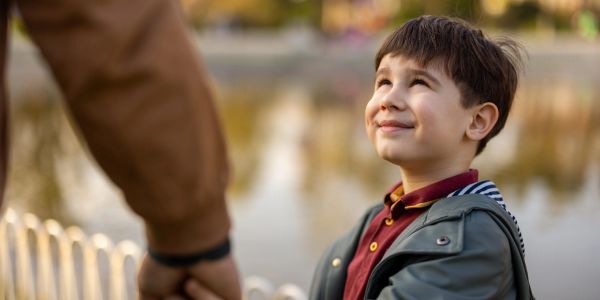 A young boy smiling while holding an adult's hand outdoors.