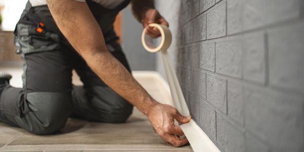 Man applying masking tape along wall.