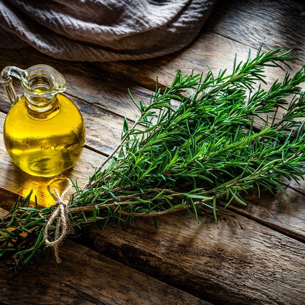 Rosemary oil in a jar next to fresh rosemary on a table