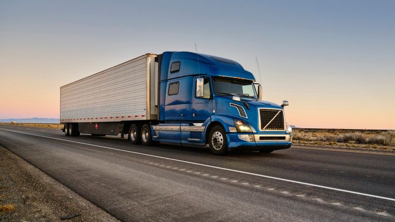 Large semi truck hauling freight on the open highway in the western USA at sunrise.