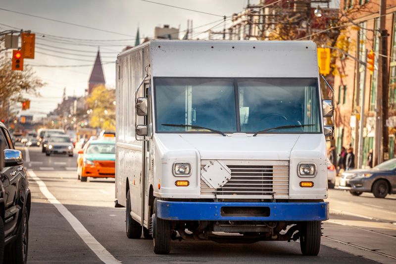 Picture of a white delivery van of a parcel delivery service in a North american street, busy.
