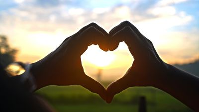 Hands forming a heart shape against a sunset.