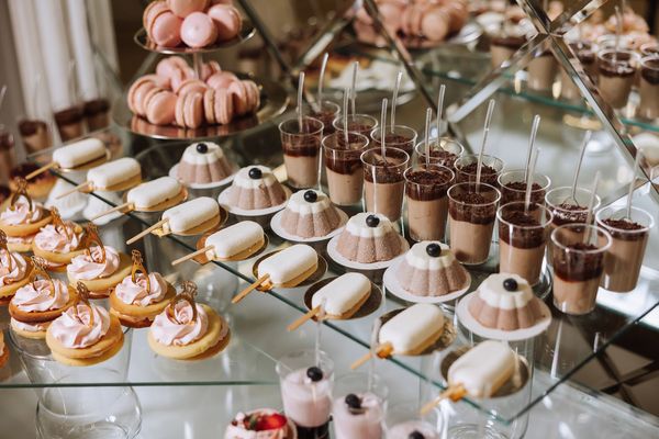 Elegant dessert display with macarons, mousse cups, and pastries on glass shelves.