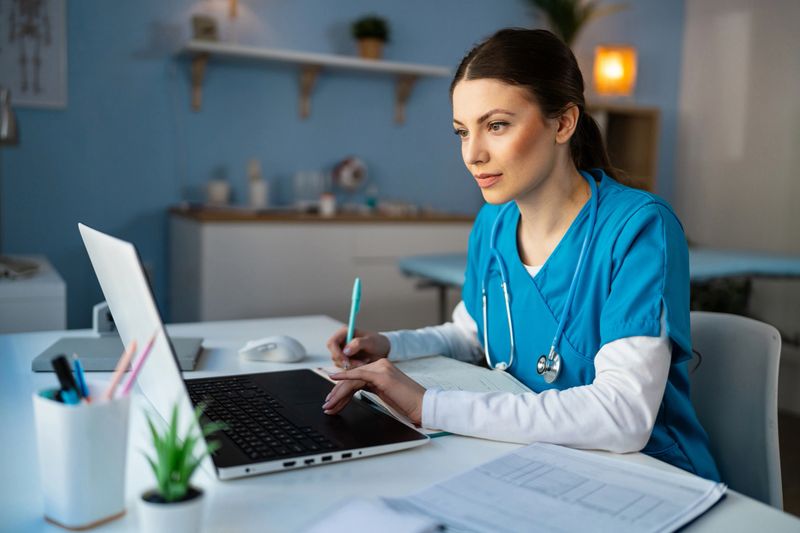 Young Caucasian female doctor or a nurse in a blue medical scrubs, working on the laptop at the modern ordination