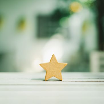 A wooden star shape standing on a white surface with a blurred background.