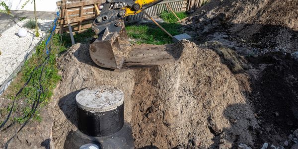 Excavator digging soil around a concrete structure in a garden.