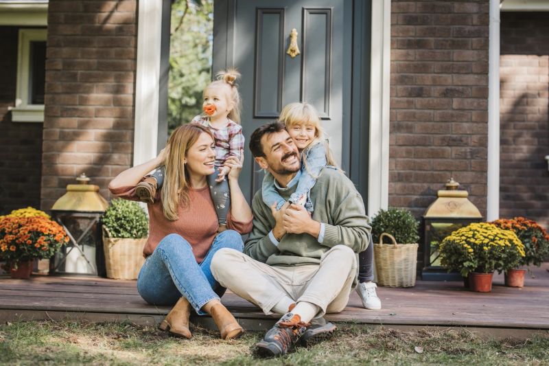Young family with two kids having fun in front of there house. Porch is decorated with flowers.