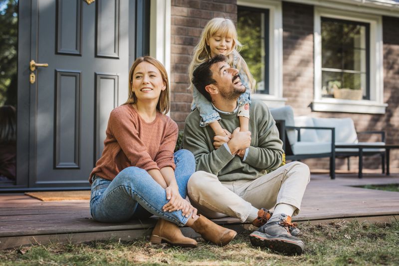 Young family with little girl having fun in front of there house. Porch is decorated with flowers.