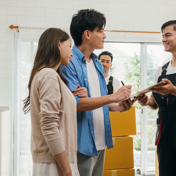Couple signing documents with delivery workers in a bright room with boxes.