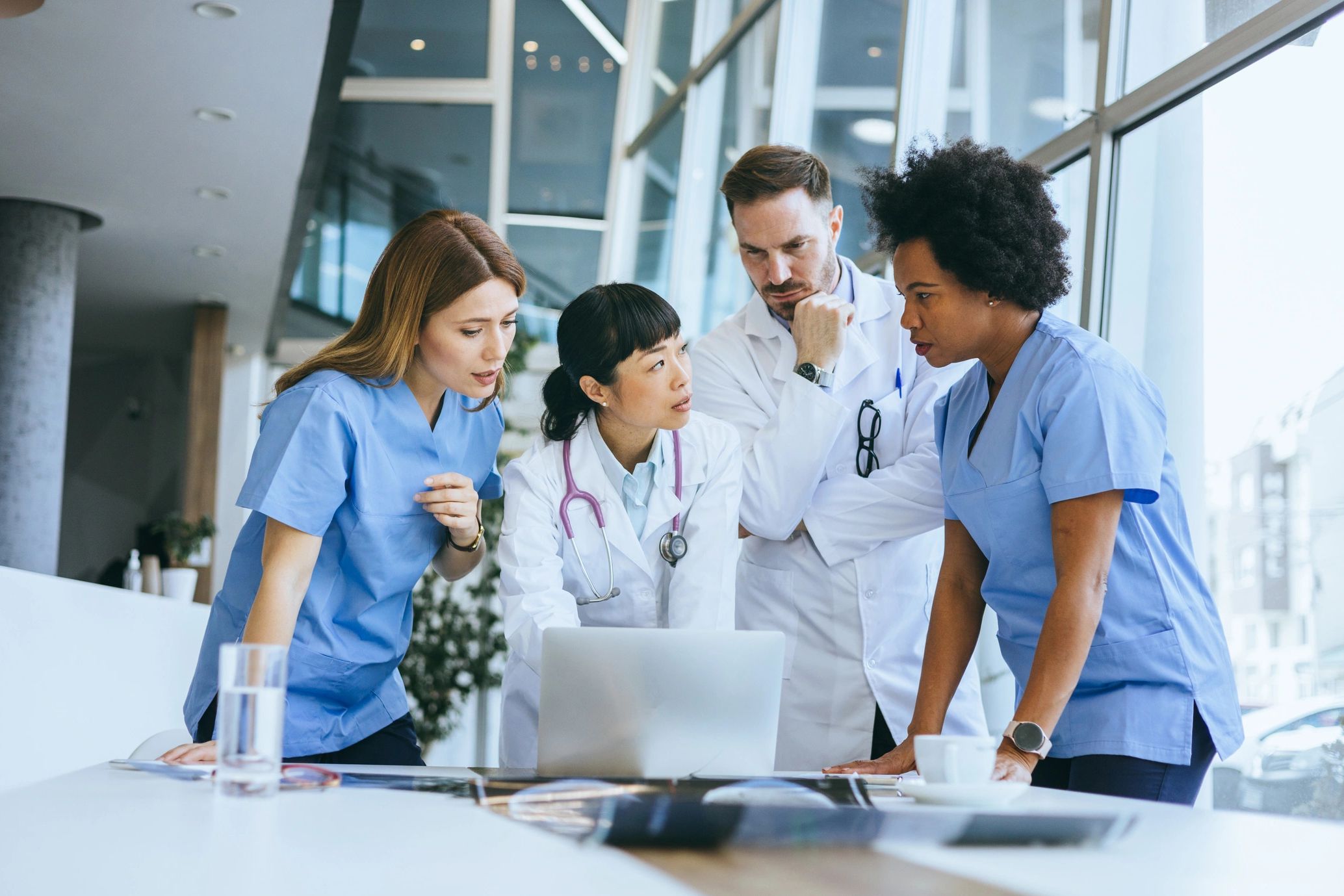 Medical team discussing patient data around a laptop in a modern hospital.
