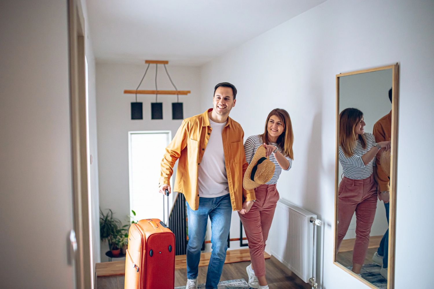 Couple entering home with luggage, smiling and holding hands.