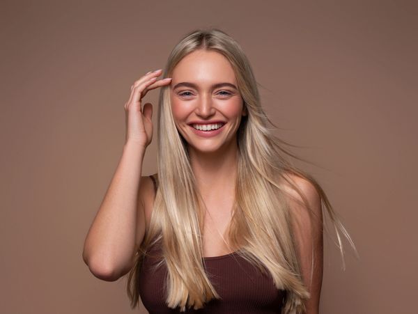 Smiling blonde woman with long hair posing against a brown background.