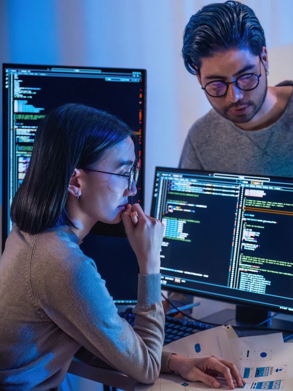 Two programmers discussing code on multiple screens.
