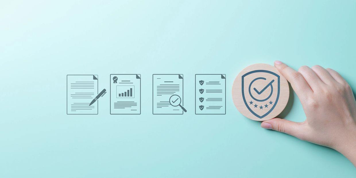 Mint green background with documents and pens, person's hand holding a badge with a check mark.