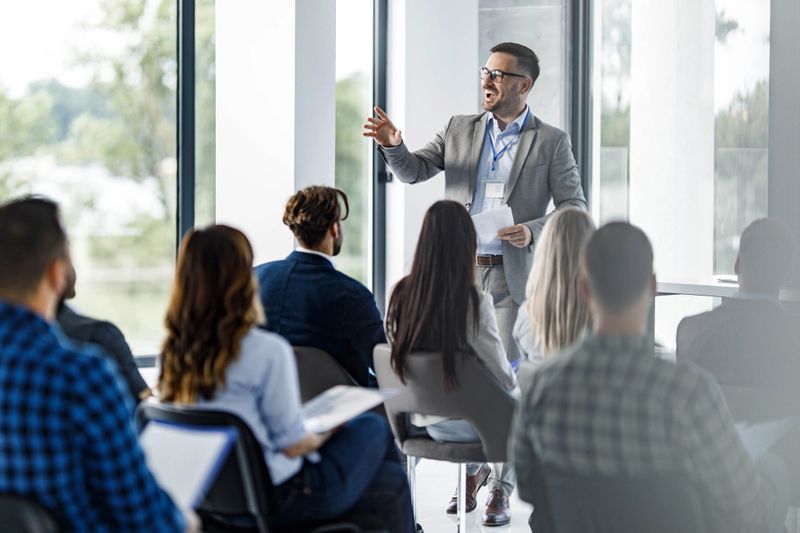 Happy CEO communicating with large group of his colleagues on education event in board room.