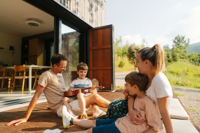 Photo of a family with two young boys, who is practicing to play an ukulele, on a front deck of their vacation house