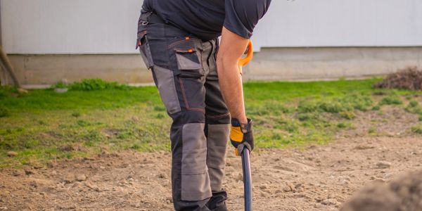 Man digging soil in a backyard with a shovel.