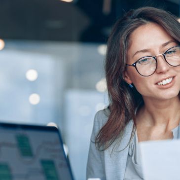 Young woman with glasses smiling while working on a laptop.