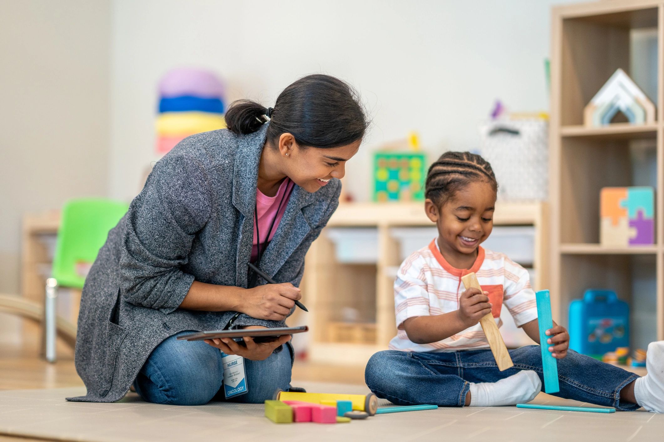 Female nurse interacting with a smiling child playing with wooden blocks.