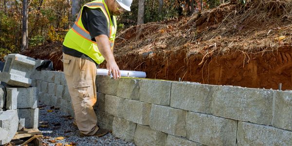 Construction worker measuring a stone retaining wall outdoors.
