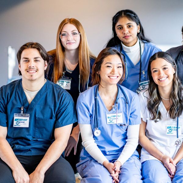 A group of diverse healthcare students smiling together in scrubs.