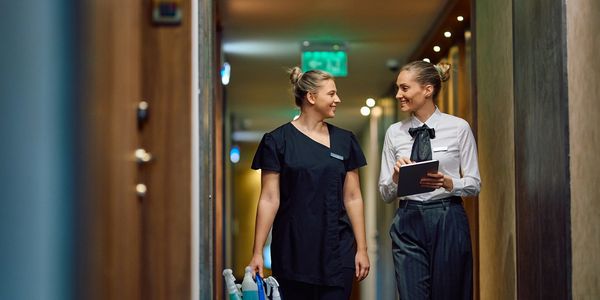Two female hospitality staff walking and chatting in a hallway.
