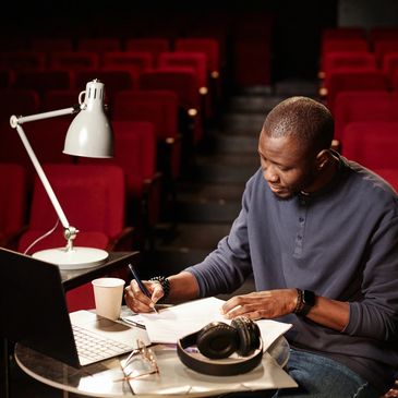 Man studying with laptop and papers in a theater with red seats.