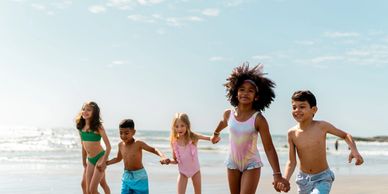 6 children of various ages and ethnicities holding hands and running on the beach.
