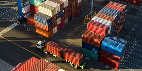 Aerial view of stacked shipping containers and a truck at a port.