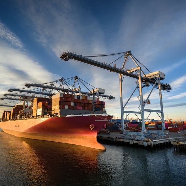Cargo ship docked with cranes at sunset.