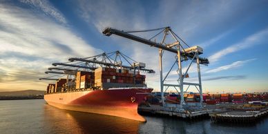 Cargo ship docked at port with cranes and containers at sunset.